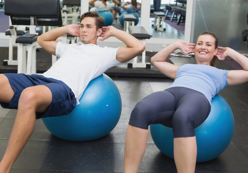 Two people are doing sit ups on exercise balls.