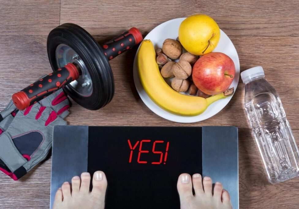 A person standing on their scale with an apple, banana and nuts.